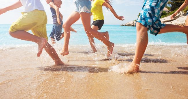 Kids feet running on the beach on the sand and in the water 